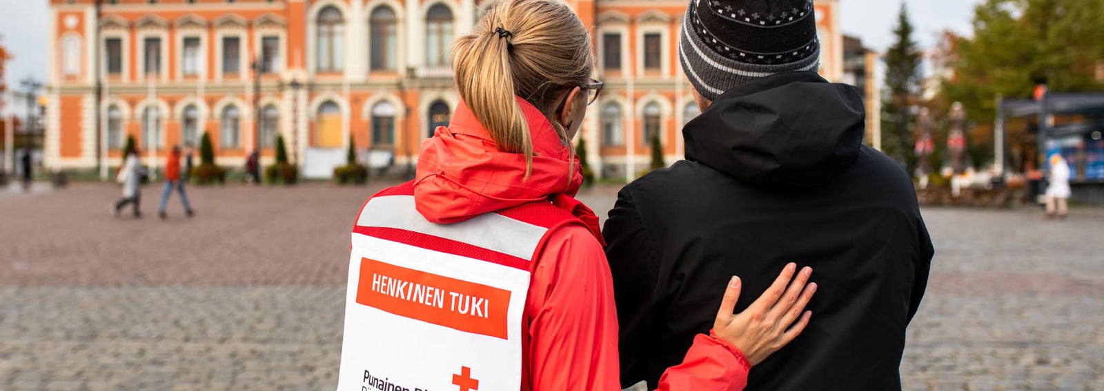 Henkilö Punaisen Ristin vapaaehtoisliiveissä keskustelee järkyttyneen miehen kanssa Kuopion torilla.