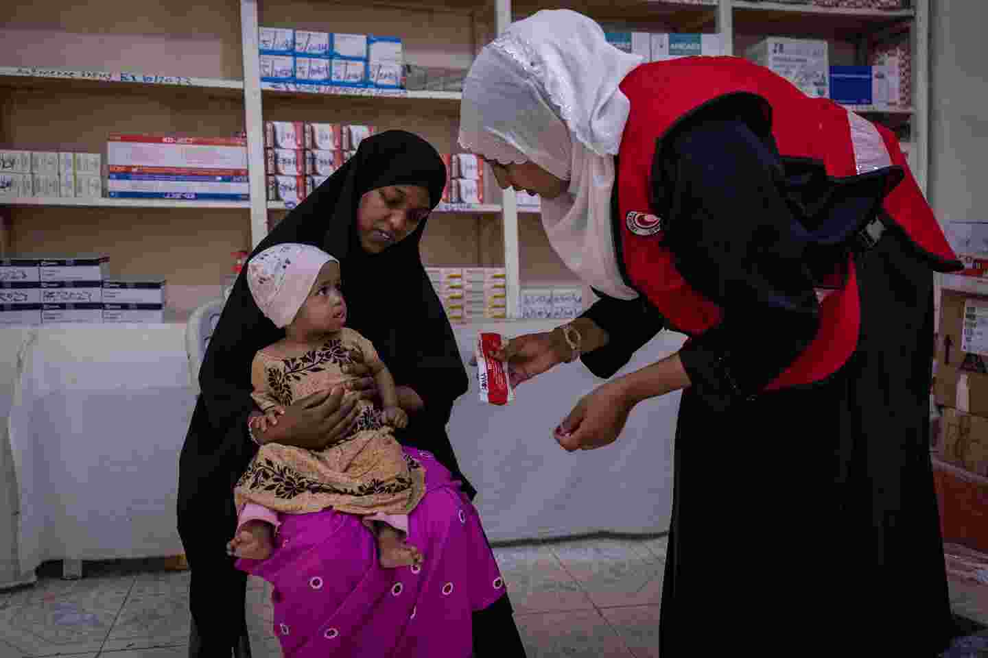 Lapsi ja äiti Punaisen Puolikuun klinikalla. Hoitaja antaa lapselle ruokaa.