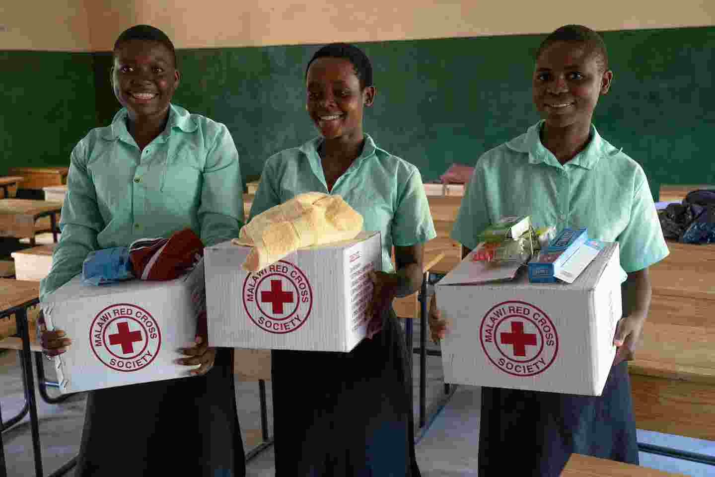 Hymyileviä koululaistyttöjä hygieniapakettien kanssa.