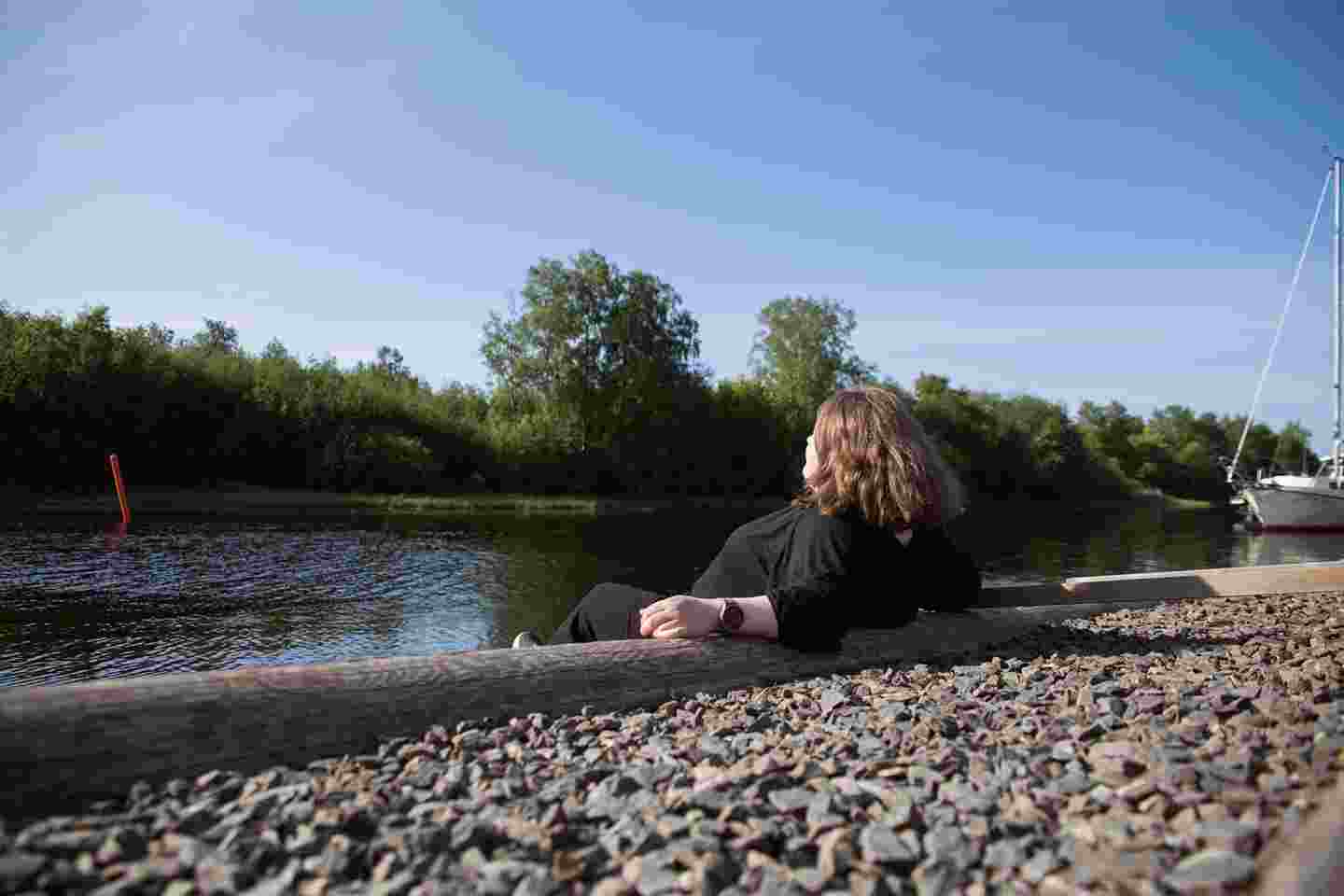 Henkilö istuu joen ääressä.