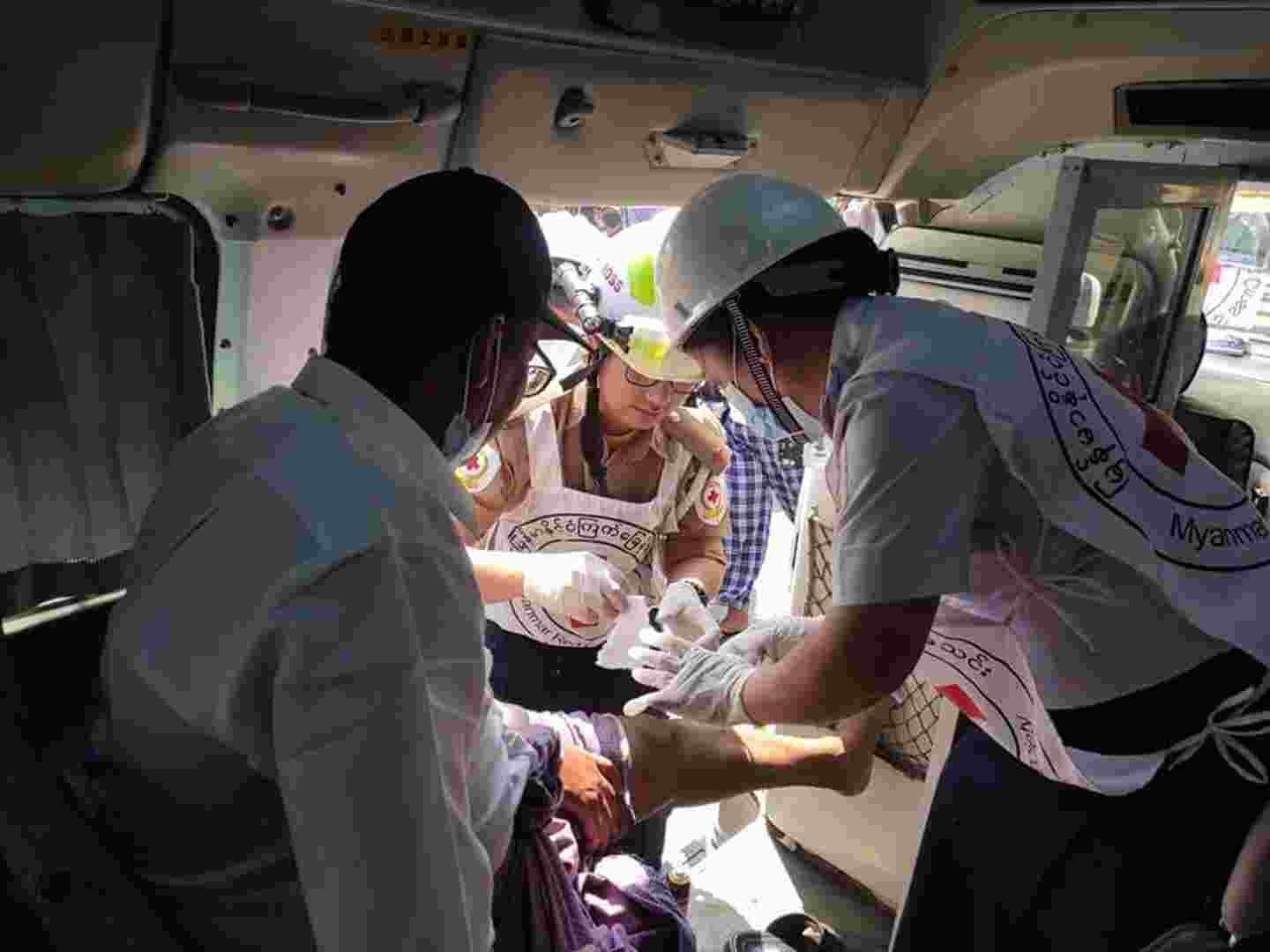 Myanmarin Punaisen Ristin vapaaehtoiset sitovat loukkaantuneen miehen jalkaa ambulanssissa.