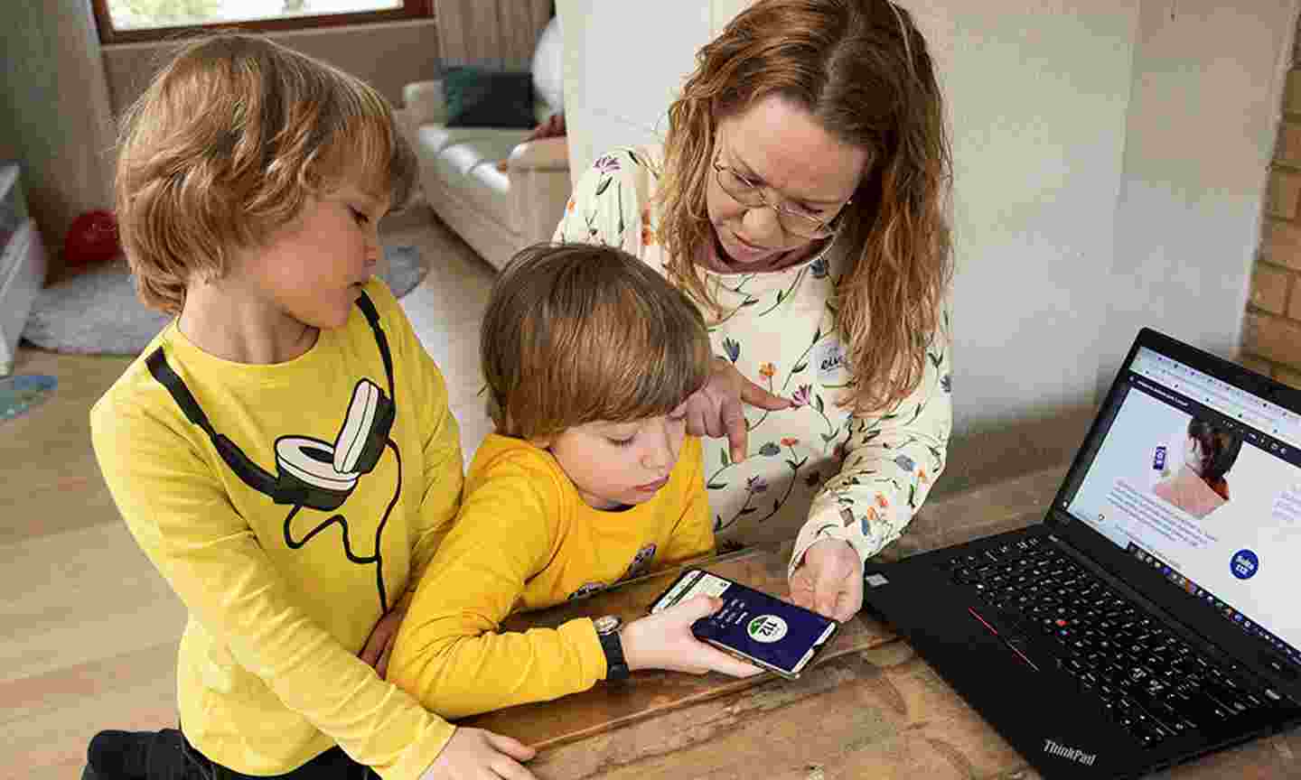 Kaksi leikki-ikäistä poikaa ja äiti tutkivat puhelinta, jossa on päällä 112-applikaatio.