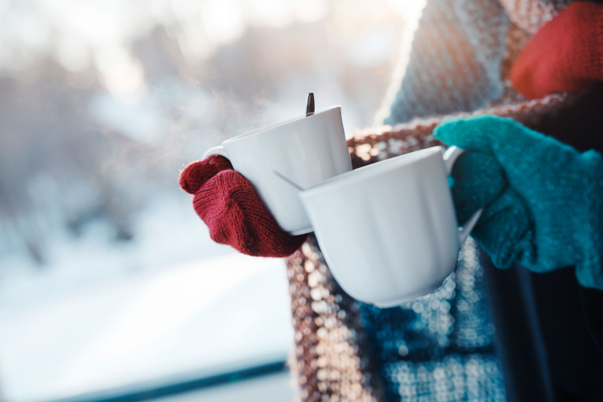 Kaksi ihmistä seisoo ulkona lapaset kädessä. Molemmat pitävät käsissään kahvikuppia.