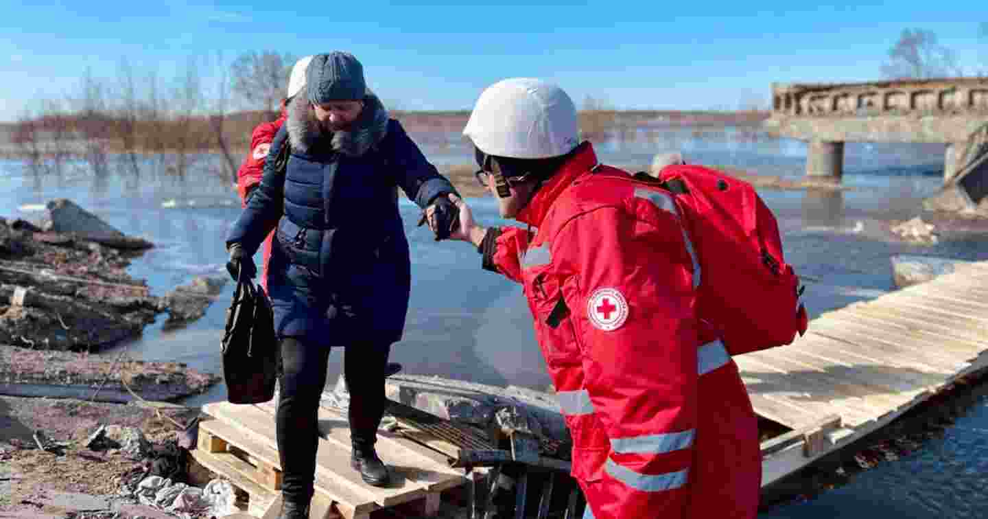 Punaisen Ristin vapaaehtoinen auttaa iäkästä henkilöä ylittämään puista siltaa.