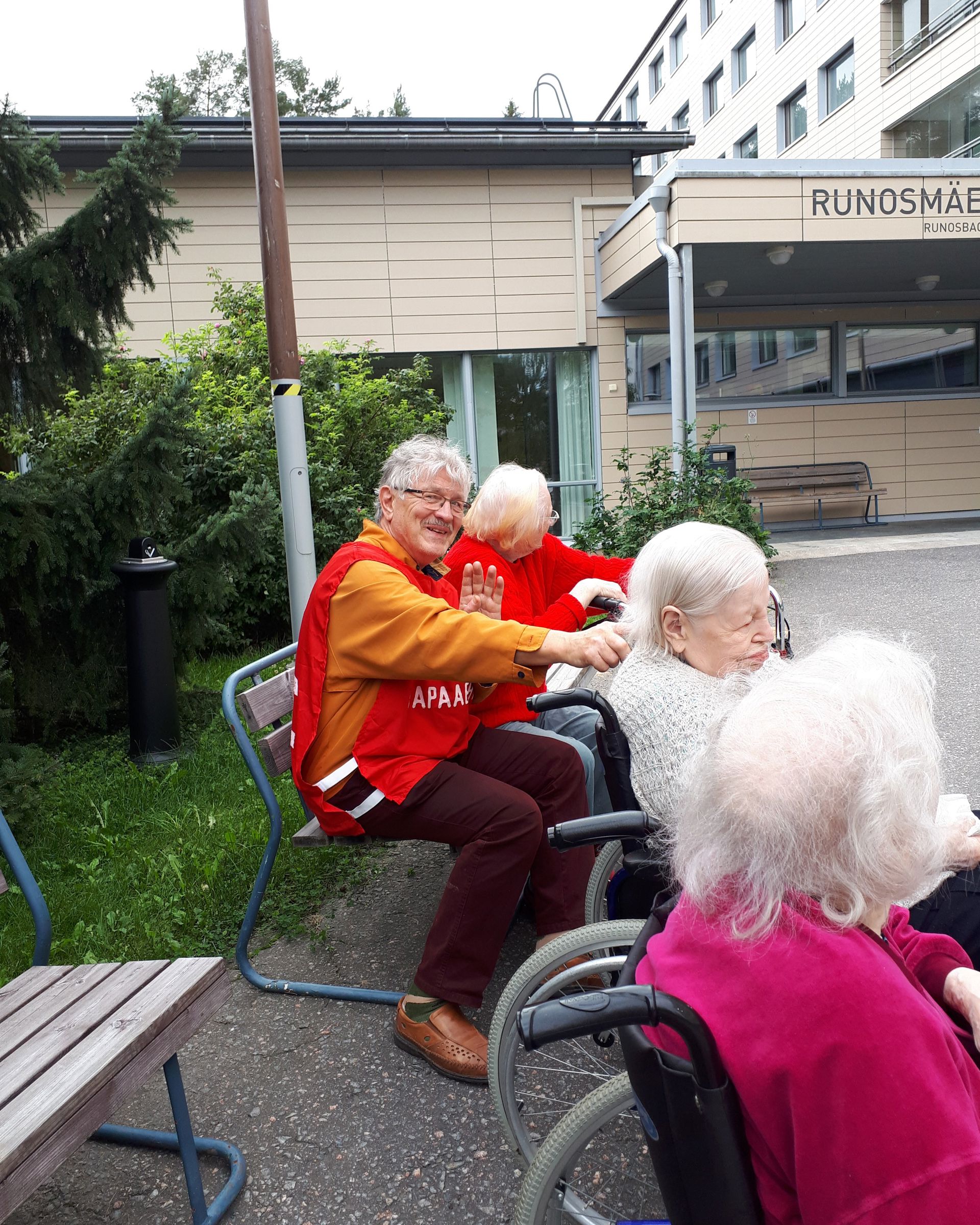 Hymyilevä Punaisen Ristin vapaaehtoinen ulkoiluttaa iäkkäitä palvelutalon asukkaita.