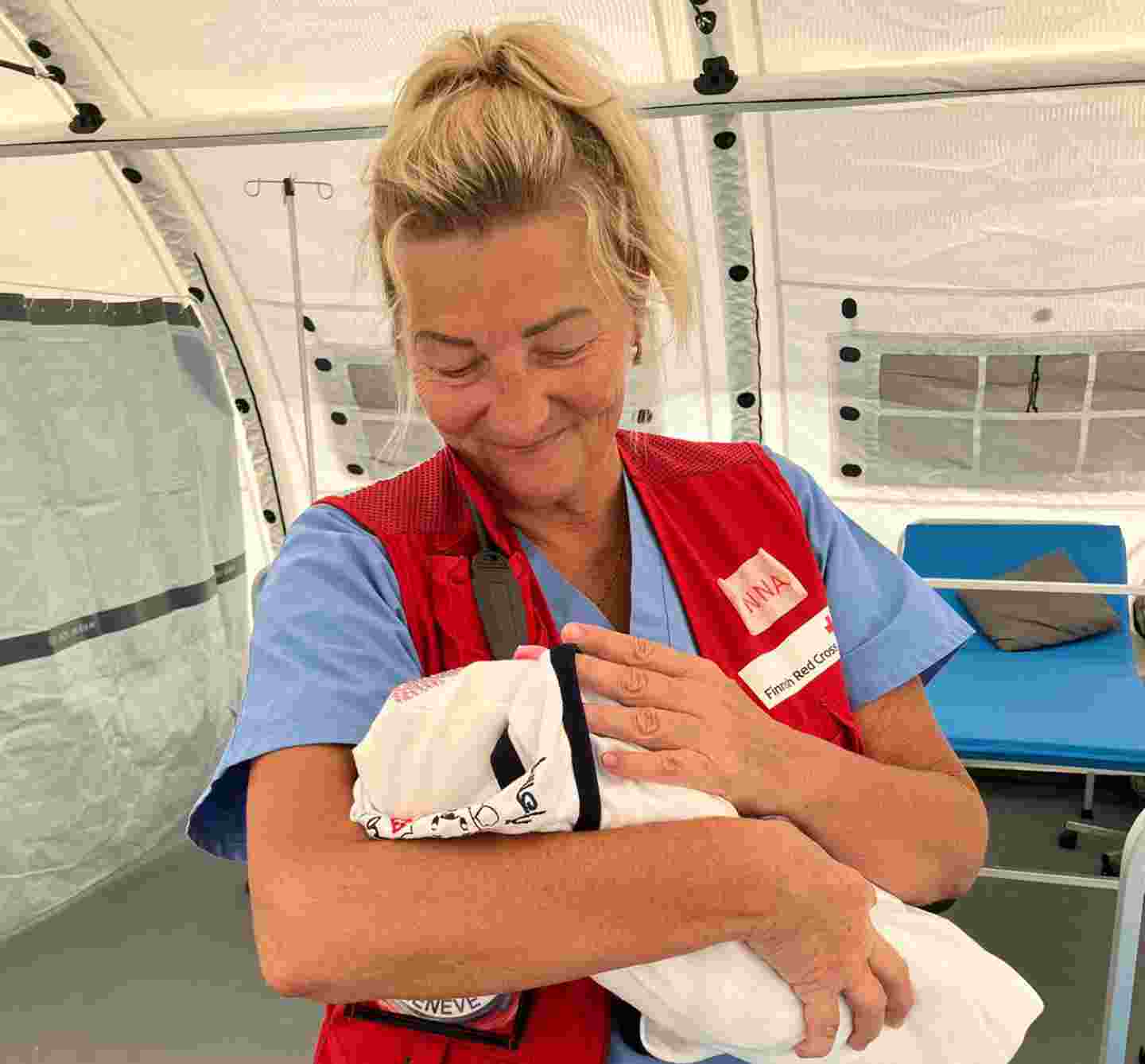 Avustustyöntekijä Minna Vanhatalo pitelee hymyillen sylissään vastasyntynyttä vauvaa.