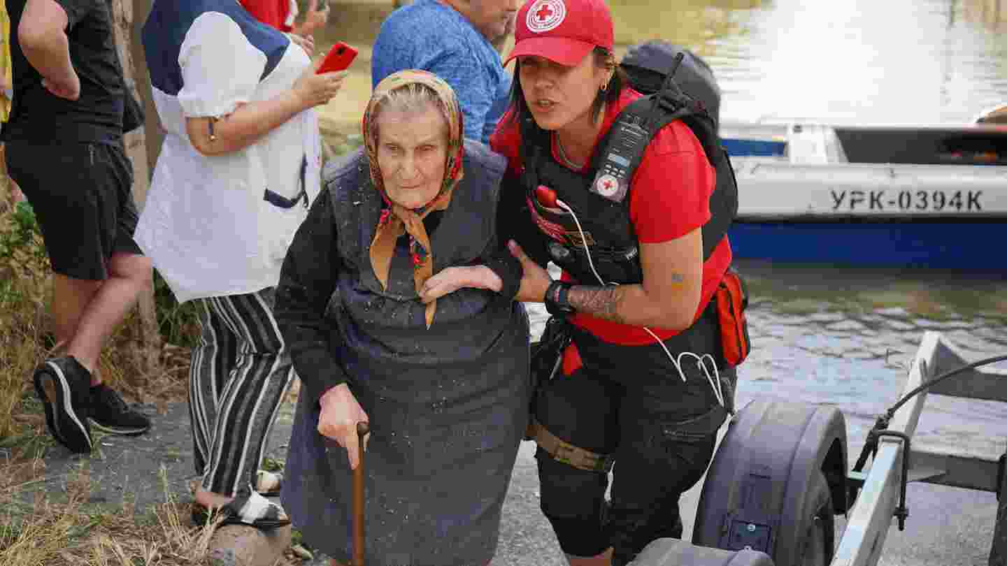 Ukrainan Punaisen Ristin työntekijä auttaa iäkästä henkilöä veden äärellä.