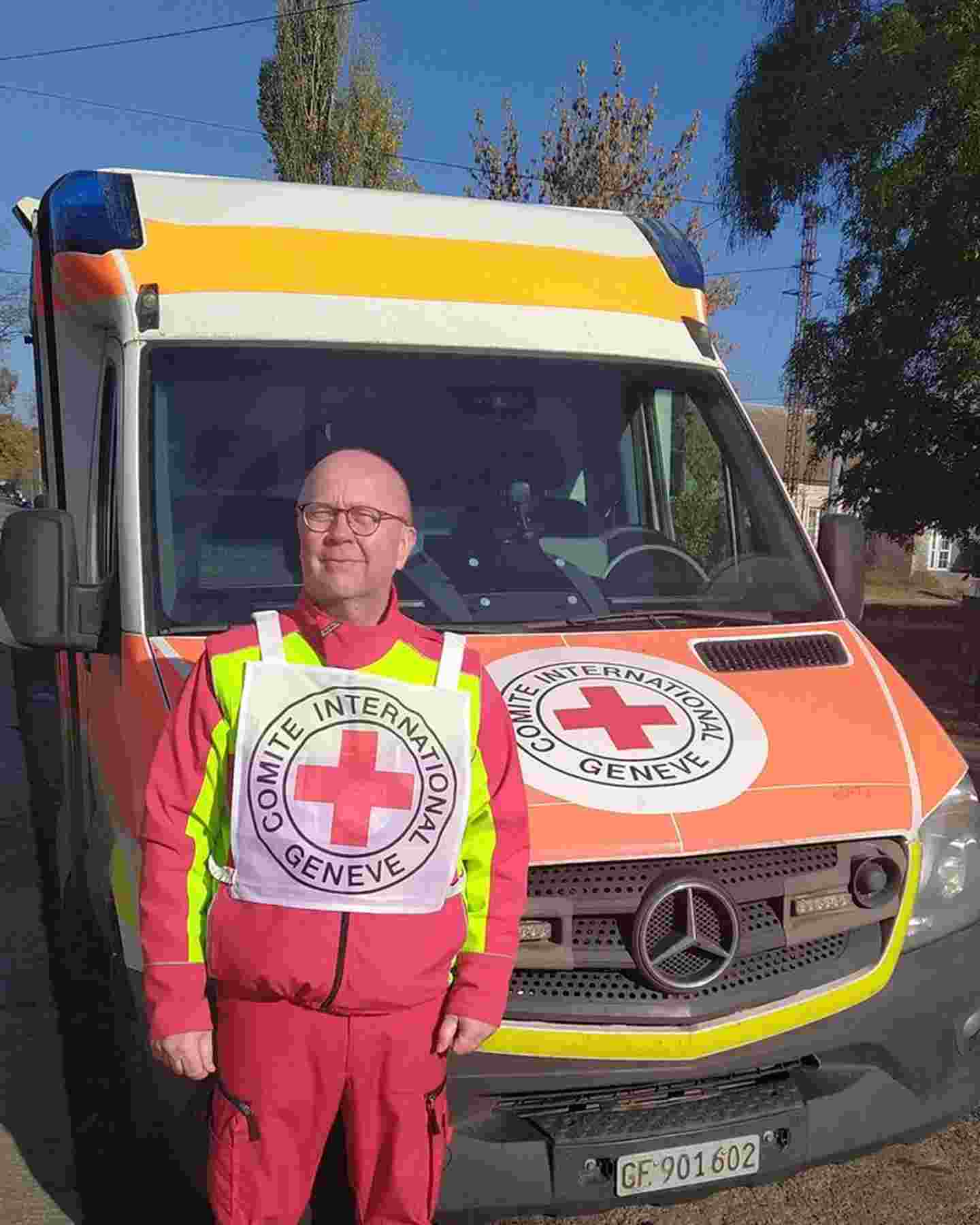 Ensihoitaja Tuomo Hämäläinen hymyilee Punaisen Ristin komitean ambulanssin vieressä