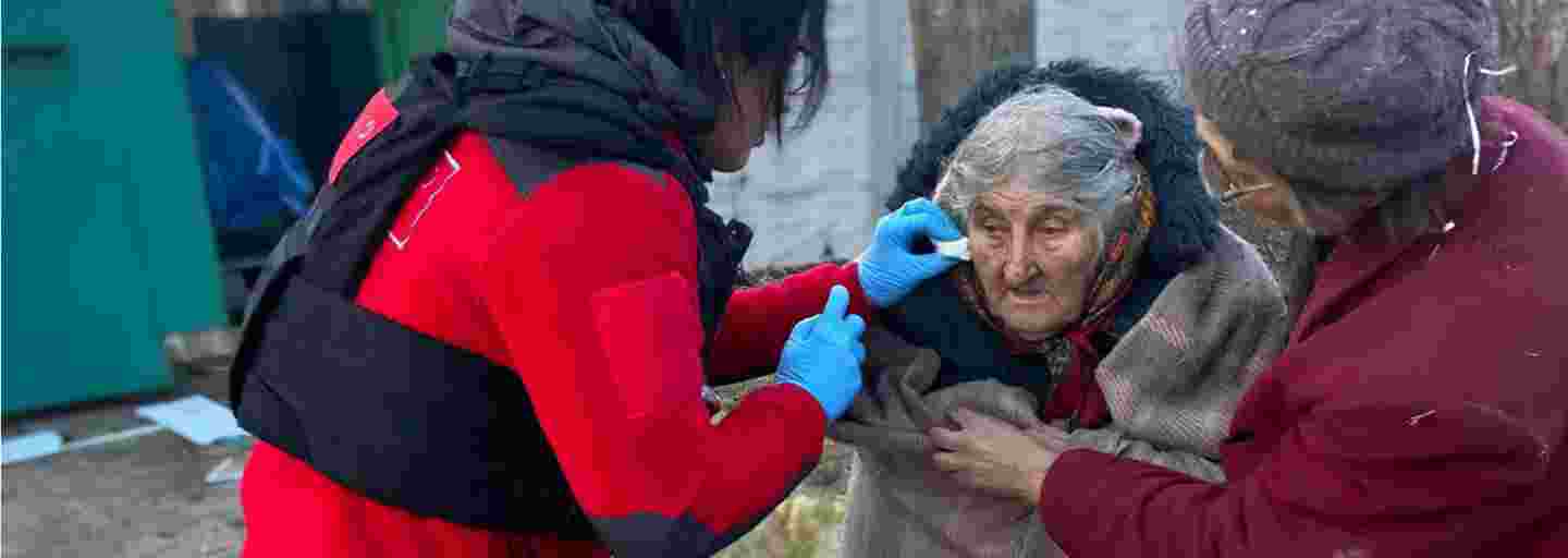 Ukrainan Punaisen Ristin vapaaehtoinen auttaa iäkästä naista kävelemään.