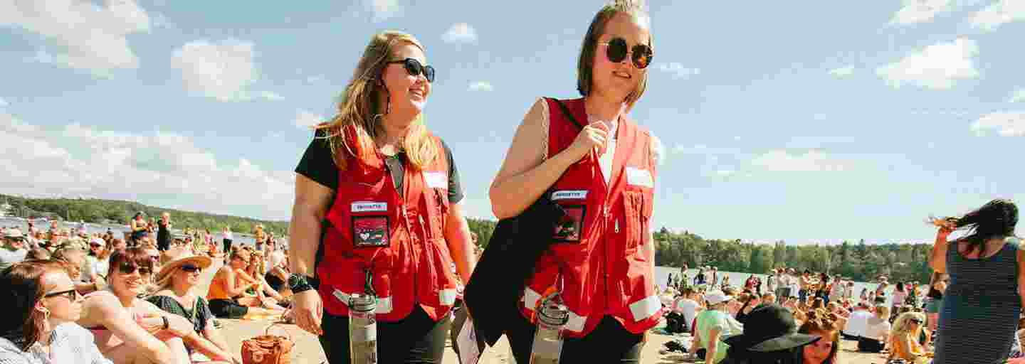 Kaksi nuorta Punaisen Ristin vapaaehtoisliiveissä suorittaa ensiapupäivystystä aurinkoisessa Ruisrockissa.