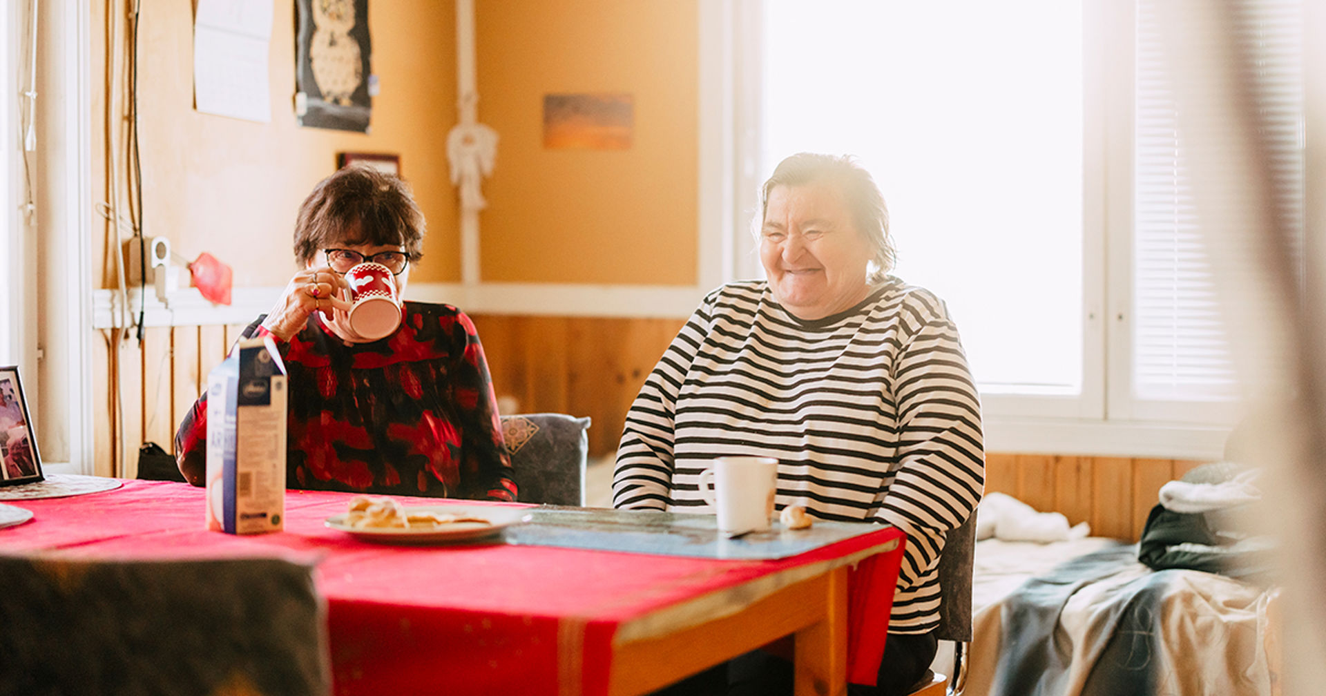 Marita ja Pirjo istuvat keittiön pöydän ääressä ja nauravat