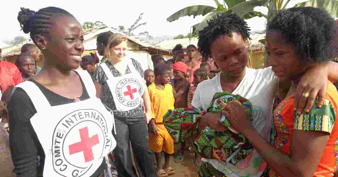 Kaksi Punaisen Ristin vapaaehtoista ja kolmas henkilö lohduttavat surevaa ihmistä.