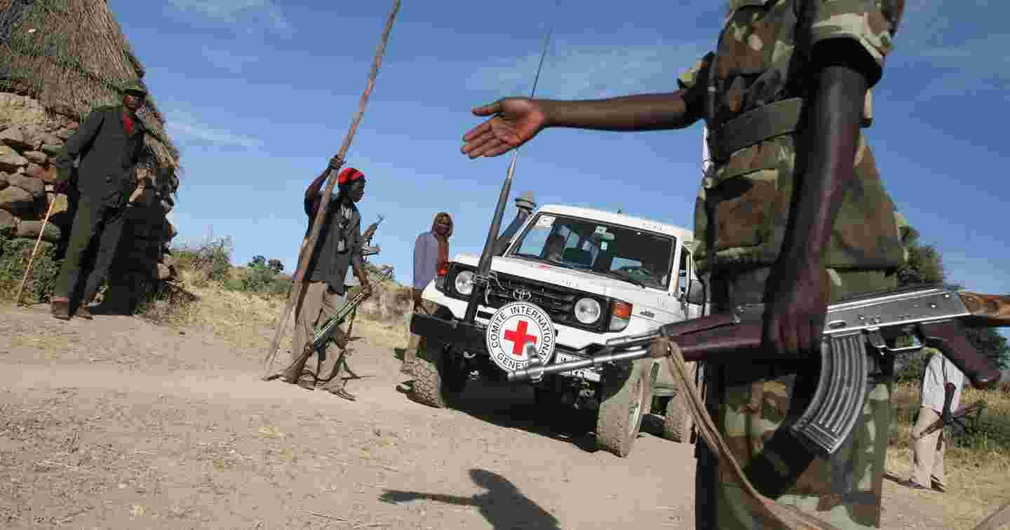 Sotilasunivormuinen henkilö kivääri kädessään ohjaa Punaisen Ristin kansainvälisen komitean autoa eteenpäin tarkastuspisteeltä.