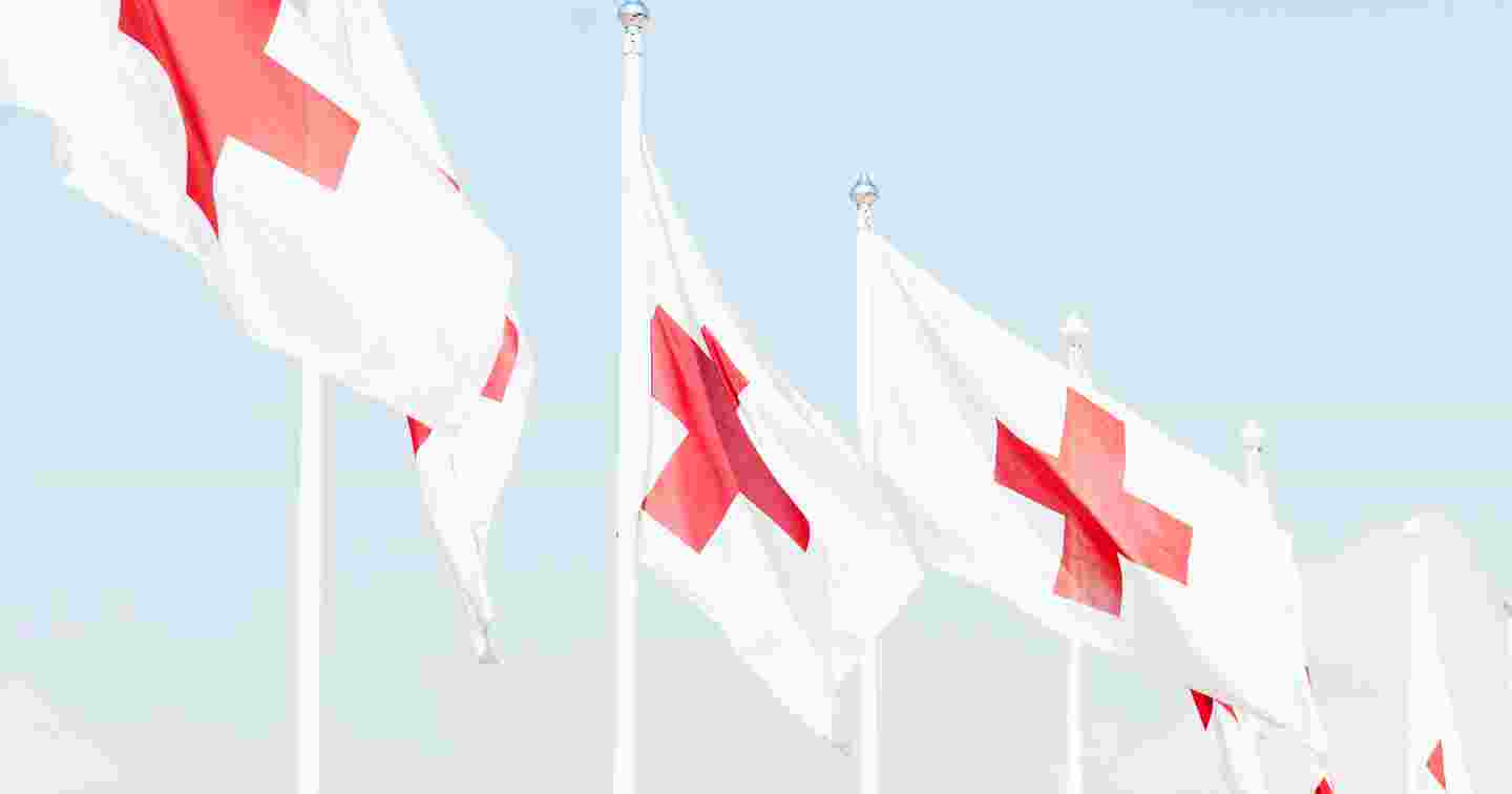 Kuusi Punaisen Ristin lippua lipputangoissa sinistä taivasta vasten.
