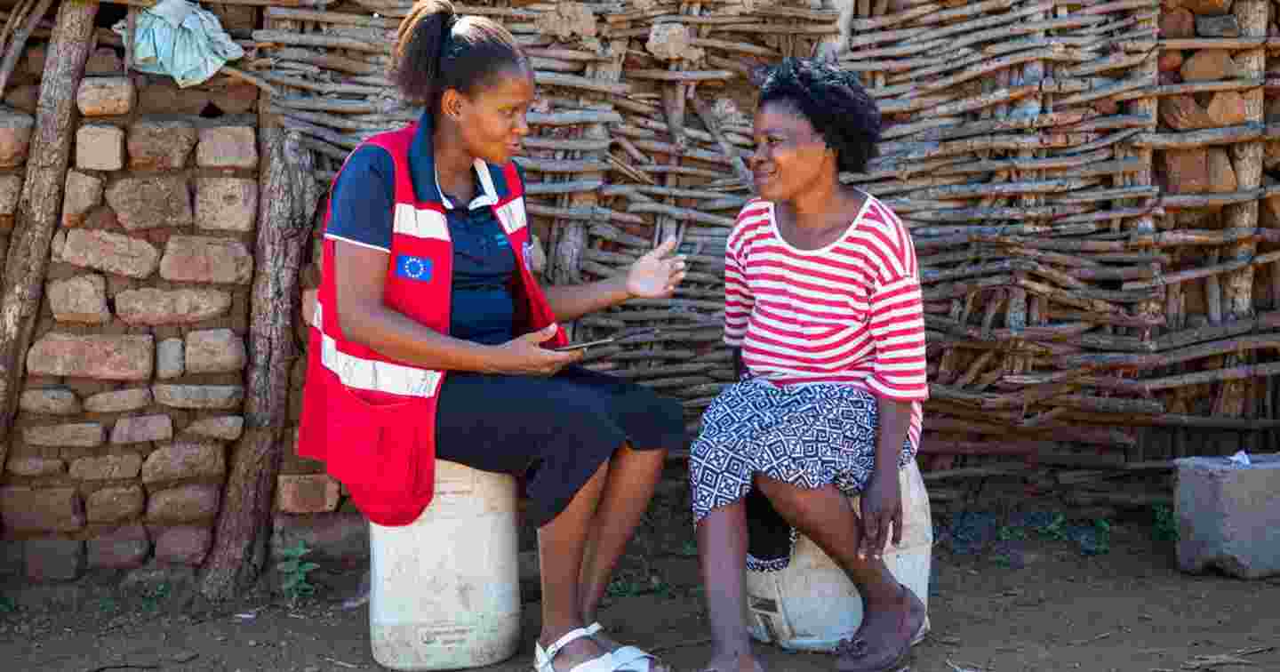Punaisen Ristin vapaaehtoinen keskustelee henkilön kanssa talon edessä.