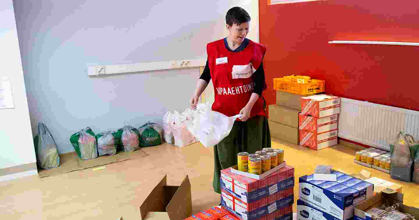 Henkilö Punaisen Ristin vapaaehtoisliiveissä pakkaa ruokatarvikkeita hymyillen.
