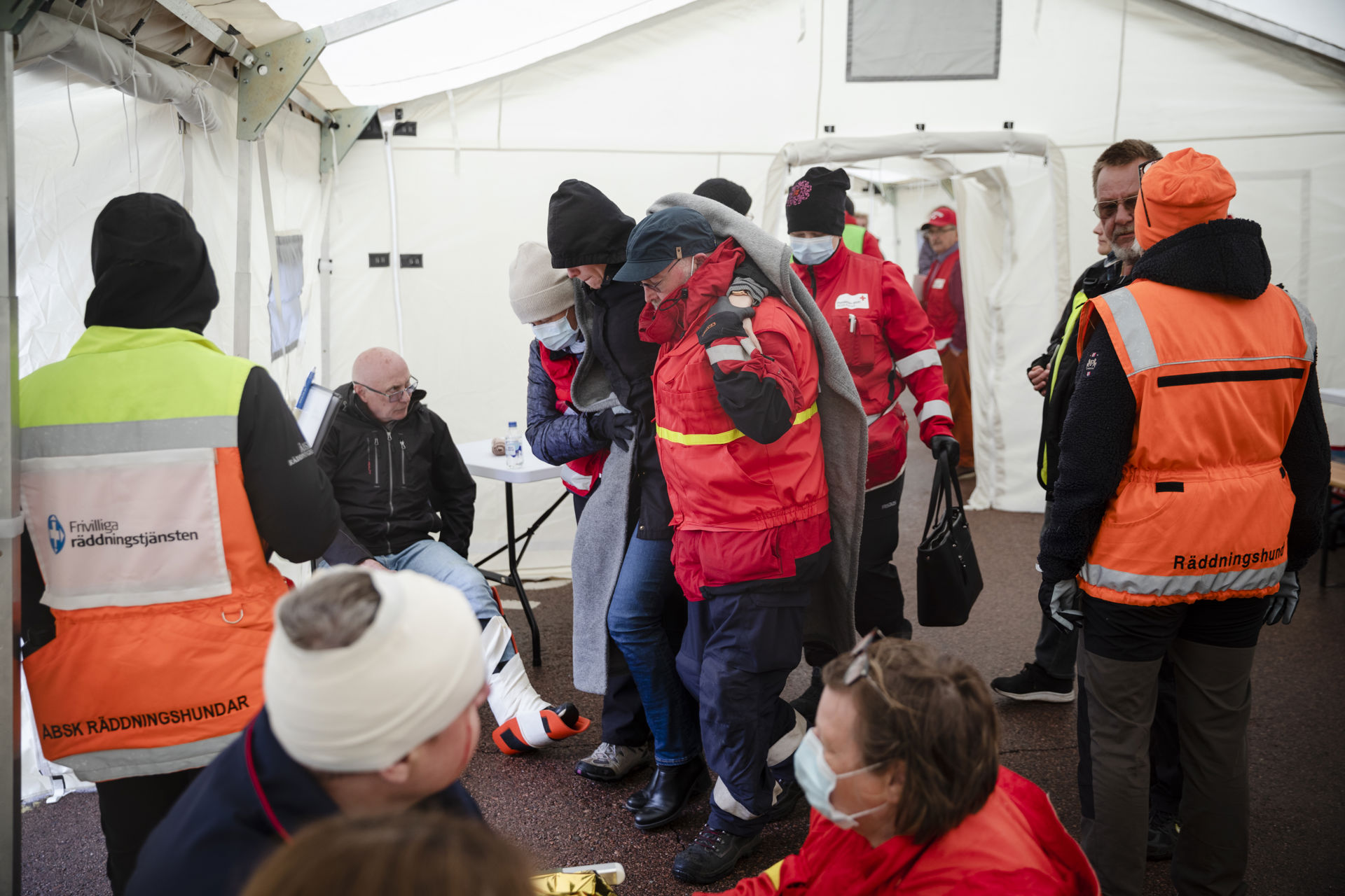 Vapaaehtoisia teltassa keskutelemassa. Vapaaehtoisten joukossa myös maalihenkilö, jonka jalka on paketissa.