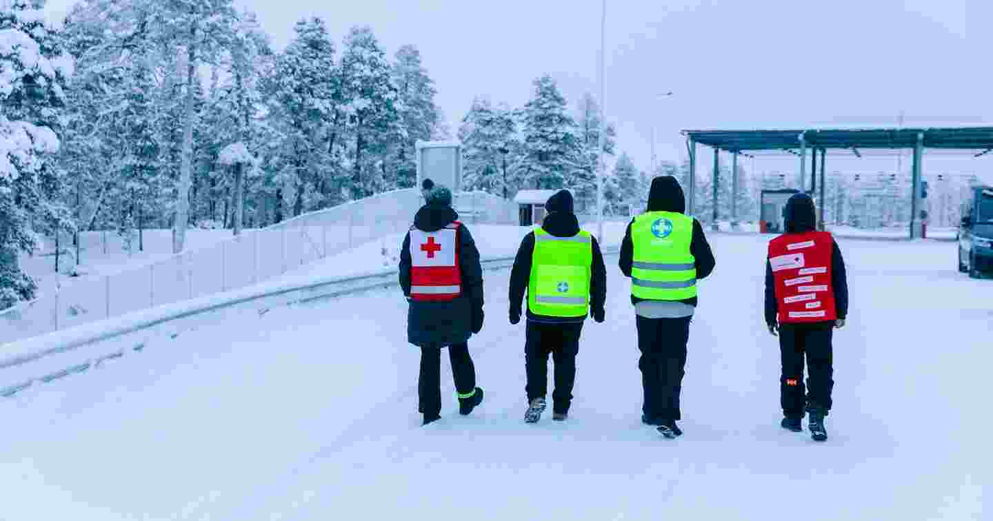 Kaksi Punaisen Ristin ja kaksi Vapaaehtoisen pelastuspalvelun vapaaehtoista kävelee kohti raja-aluetta talvisessa säässä.